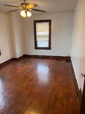 an empty room with wooden floor chandelier fan and windows