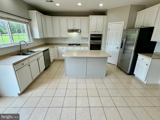 a kitchen with stainless steel appliances a sink a stove a refrigerator cabinets and a window