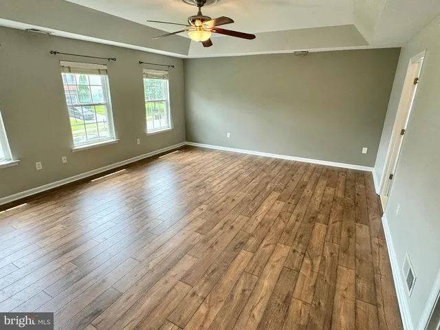an empty room with wooden floor chandelier fan and windows