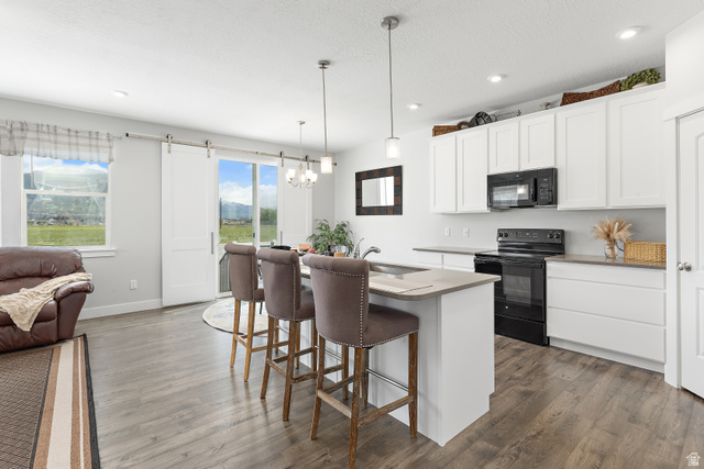 2343 Wysteria Drive Mapleton, UT 84664 - Photo 8 of 30 Kitchen featuring white cabinetry, black appliances, a kitchen breakfast bar, a kitchen island with sink, and a textured ceiling