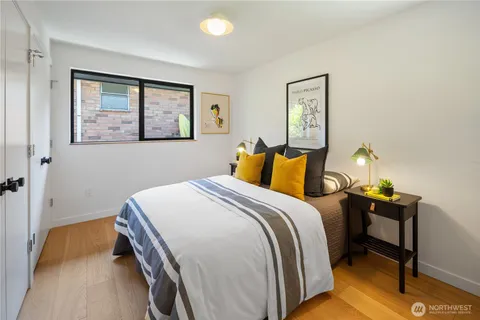 a bedroom with a bed and a lamp on dresser with wooden floor