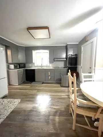 a view of a kitchen with kitchen island a sink appliances wooden floor and a counter top space