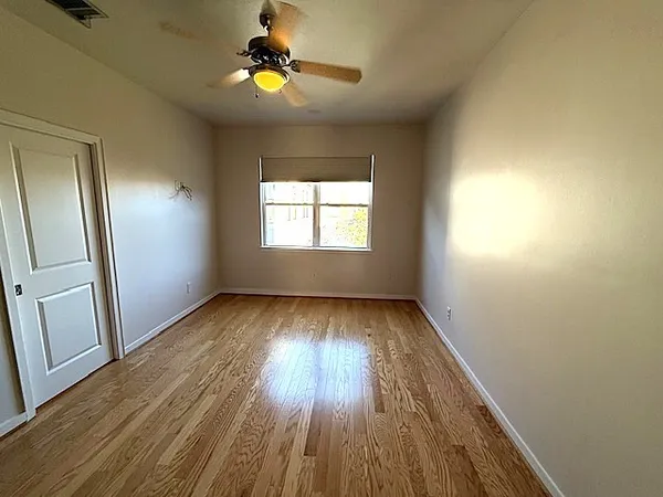 a view of empty room with wooden floor and fan
