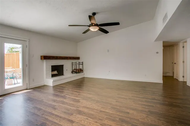 an empty room with wooden floor fireplace and windows