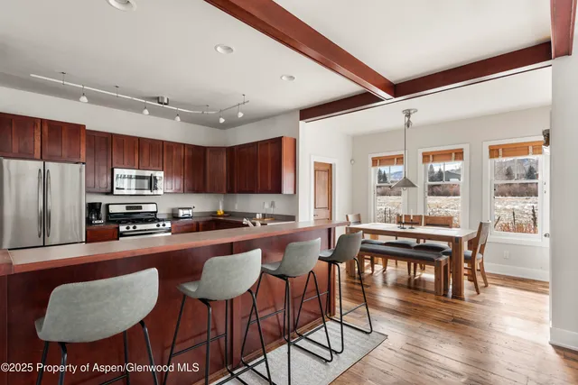 a kitchen with stainless steel appliances granite countertop a stove a refrigerator a dining table and chairs with wooden floor