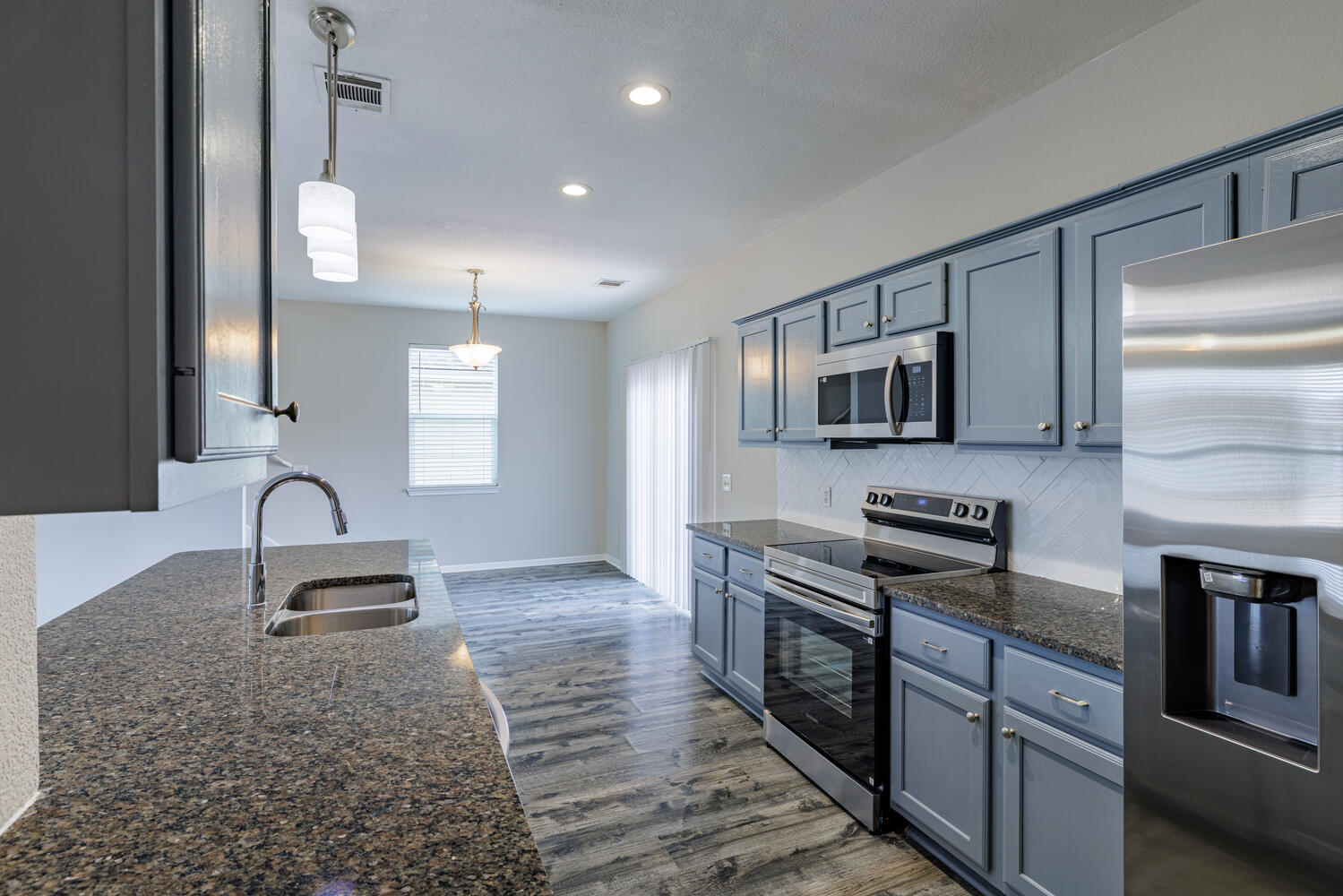 11402 Marshall Street Manor, TX 78653 - Photo 13 of 34 Kitchen featuring dark stone counters, stainless steel appliances, dark wood-type flooring, hanging light fixtures, and decorative backsplash