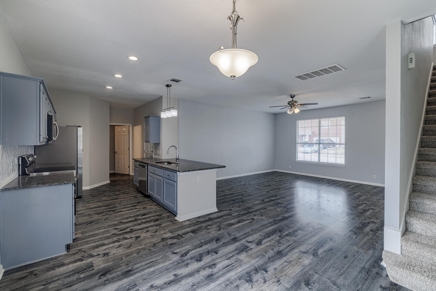 11402 Marshall Street Manor, TX 78653 - Photo 34 of 34 Kitchen featuring dark stone counters, decorative light fixtures, open floor plan, dark wood-style floors, and stainless steel microwave