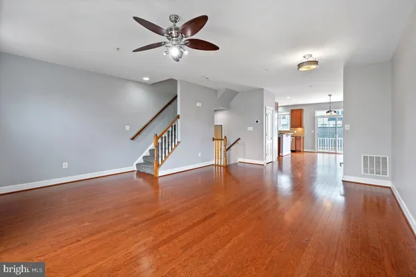 a view of an empty room with wooden floor and a ceiling fan