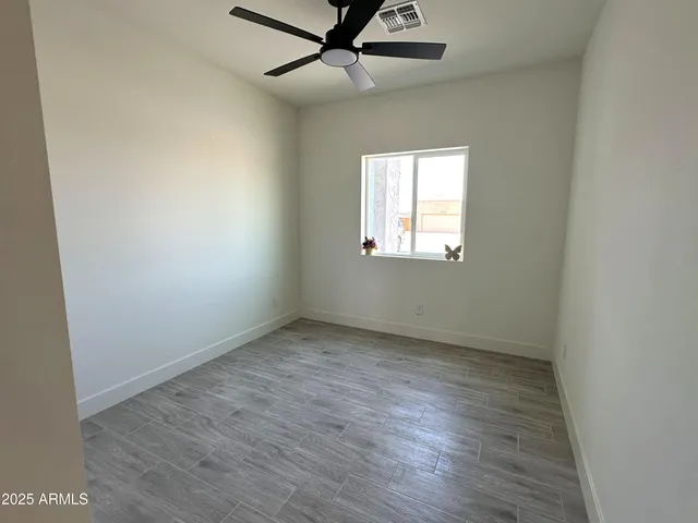 an empty room with wooden floor ceiling fan and windows