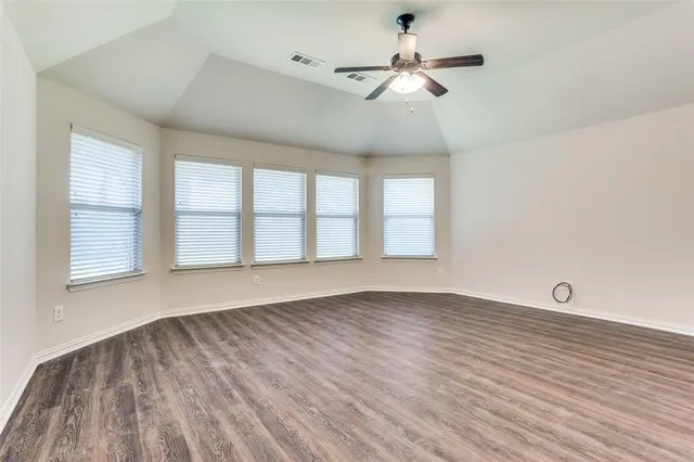 an empty room with wooden floor fan and windows