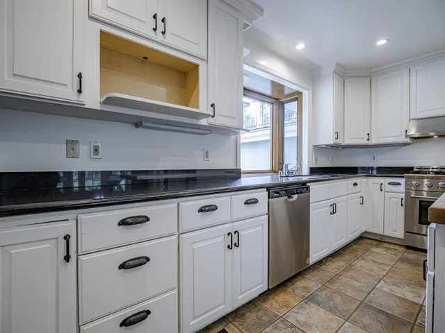 a kitchen with granite countertop white cabinets stainless steel appliances and a window
