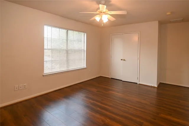 an empty room with wooden floor chandelier fan and windows