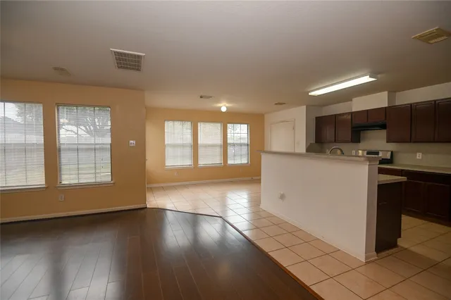 a view of an empty room with wooden floor and a kitchen