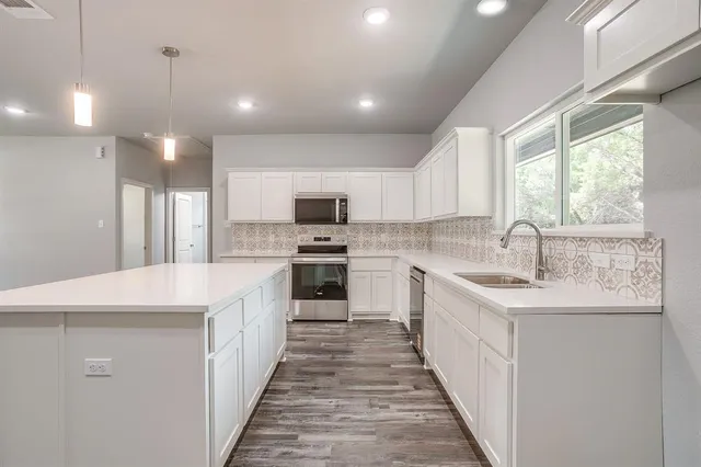 a kitchen with kitchen island granite countertop a sink appliances cabinets and a counter top space