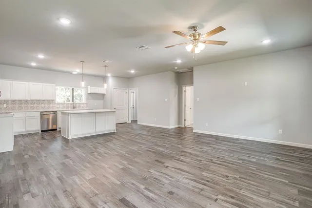 a view of an empty room with kitchen appliances and a ceiling fan