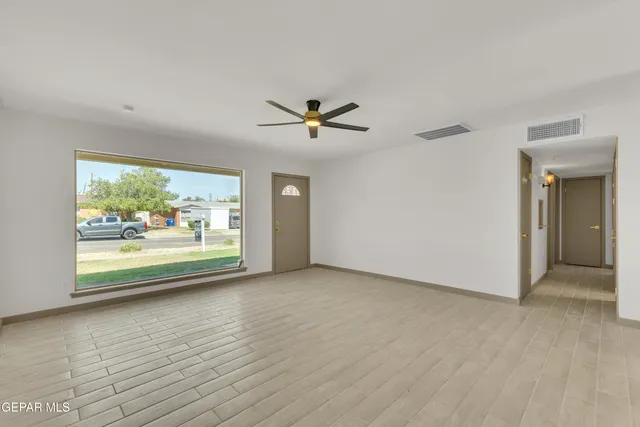 an empty room with chandelier fan and windows