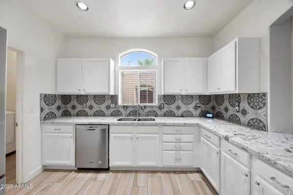 a kitchen with granite countertop a refrigerator oven a sink and white cabinets