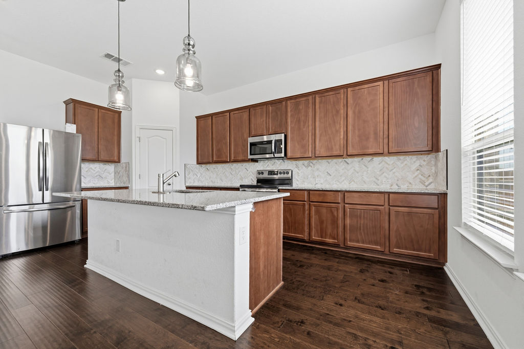 1005 Ridge Runner Drive Georgetown, TX 78628 - Photo 6 of 32 Kitchen featuring a central island with a sink, wood-finish flooring, stainless steel appliances, pendant lighting, and a white herringbone tile backsplash