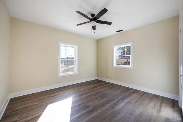 a view of an empty room with wooden floor and a ceiling fan