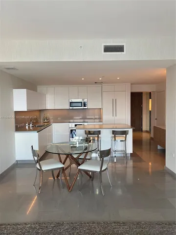 a living room with stainless steel appliances kitchen island granite countertop a dining table chairs and a refrigerator