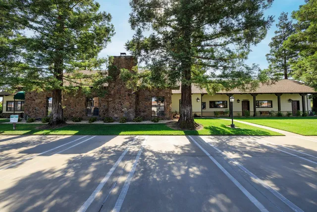 a view of a white house in front of a big yard with large trees
