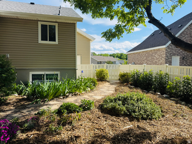 281 Winchester Drive Springville, UT 84663 - Photo 27 of 27 Landscaped backyard featuring a stone pathway, established garden beds with mulch, a white picket fence, and mature foliage