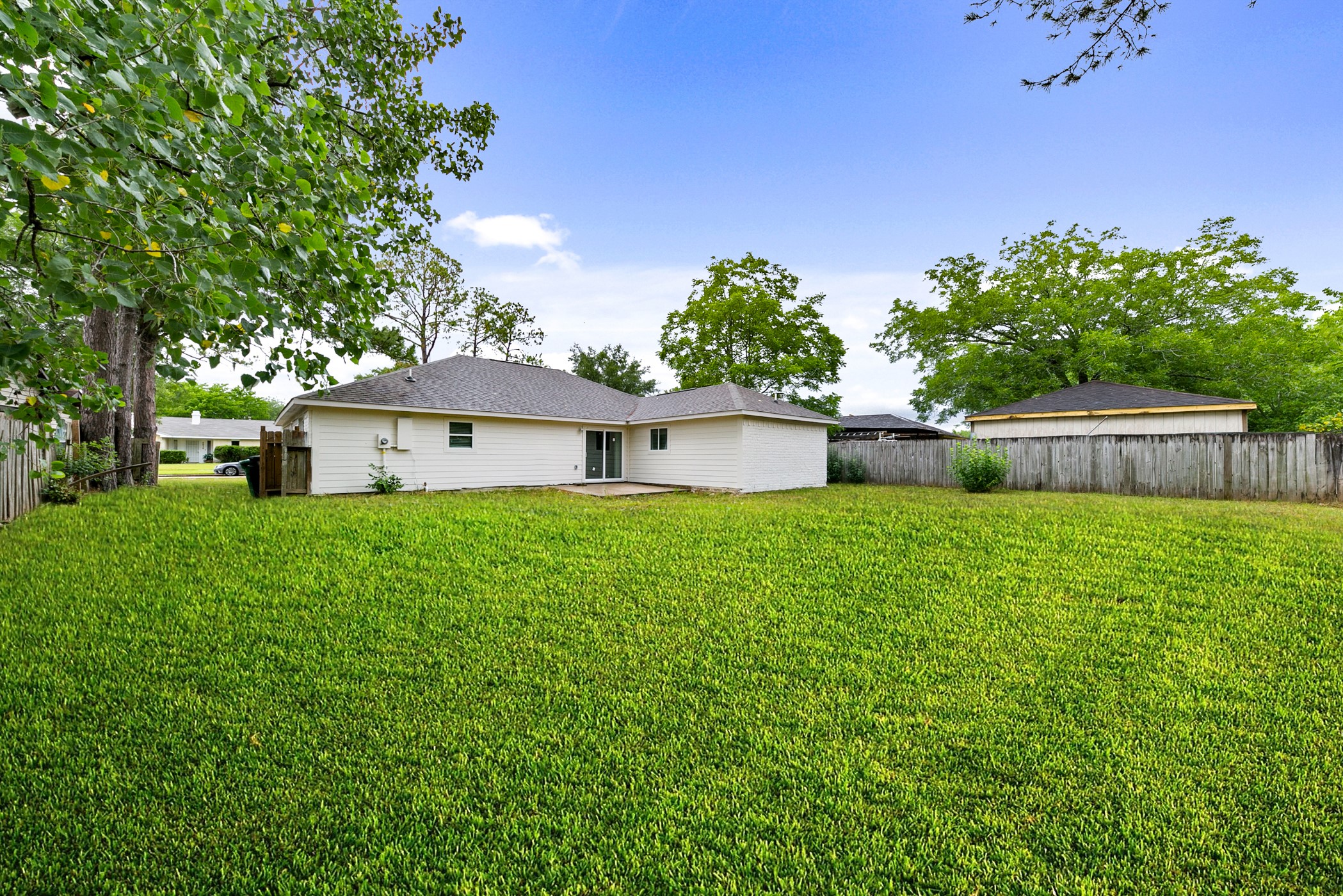6811 McCullum Road Houston, TX 77489 - Photo 21 of 22 Spacious backyard with well-maintained lawn, surrounded by a wooden fence for privacy. The home features a light-colored exterior and a small patio area, perfect for outdoor activities or relaxation.
