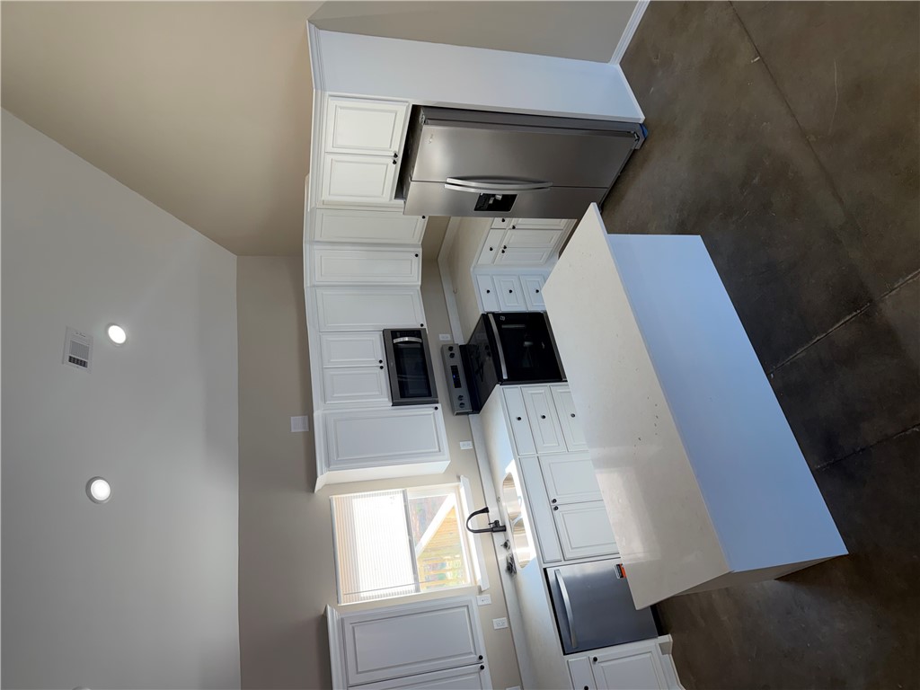 248 Southwest 4th Street Atkins, AR 72823 - Photo 13 of 14 Kitchen featuring a vaulted ceiling with recessed lighting, white cabinetry, stainless steel appliances, and a central island with a solid surface countertop