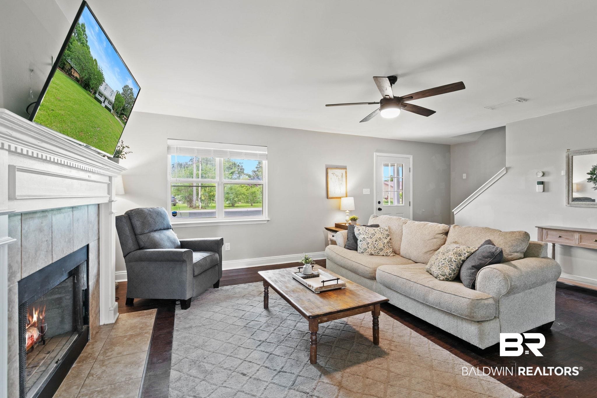 22810 High Ridge Road Fairhope, AL 36532 - Photo 21 of 78 Living area featuring a fireplace with a white mantel and tile surround, dark wood-finish flooring, a ceiling fan, a window with exterior views, and a white paneled door