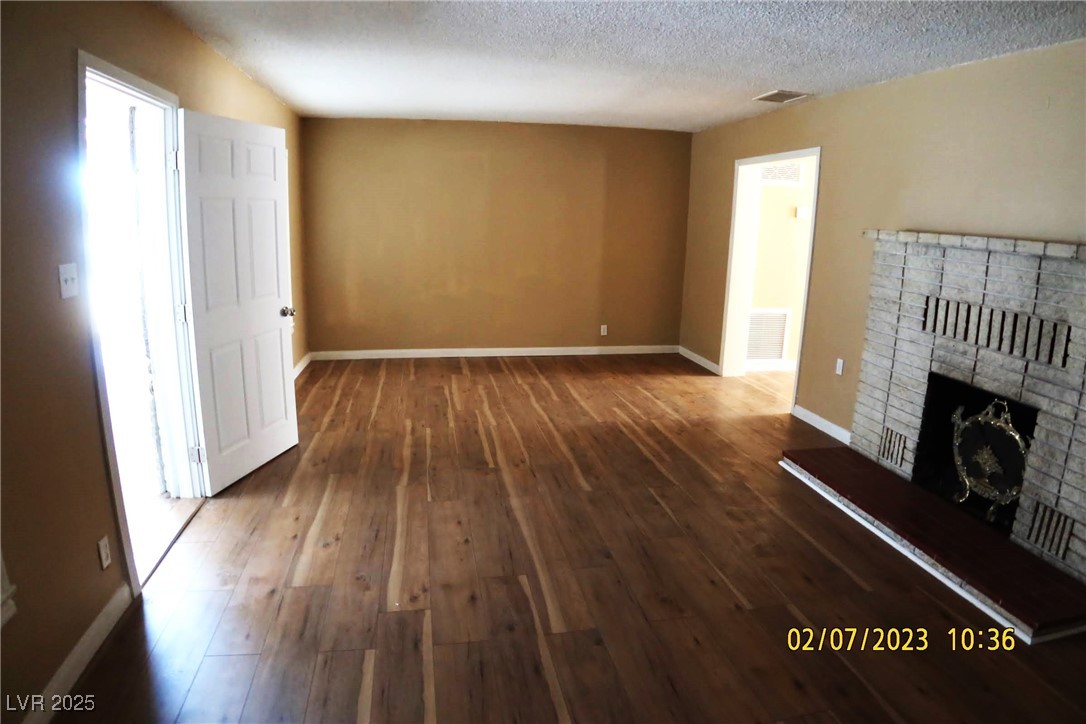 10 East Bonanza Road Las Vegas, NV 89101 - Photo 11 of 35 Unfurnished living room featuring a textured ceiling, visible vents, wood-type flooring, baseboards, and a brick fireplace