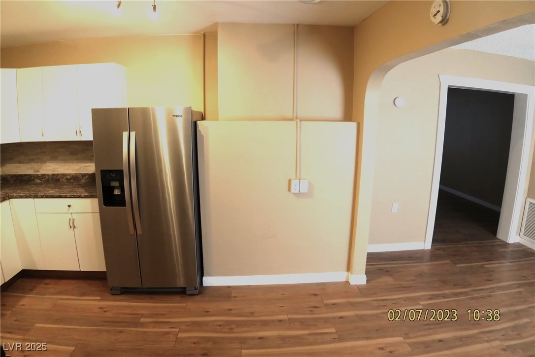 10 East Bonanza Road Las Vegas, NV 89101 - Photo 22 of 35 Kitchen with dark countertops, wood finished floors, arched walkways, stainless steel fridge with ice dispenser, and white cabinets