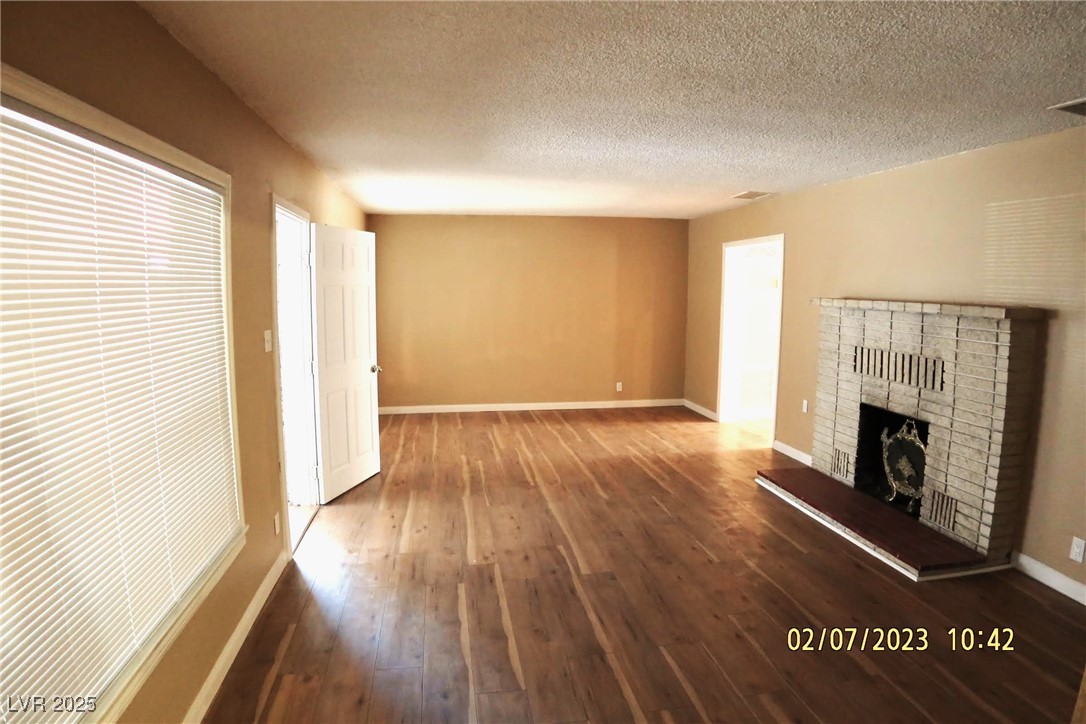 10 East Bonanza Road Las Vegas, NV 89101 - Photo 30 of 35 Unfurnished living room featuring a textured ceiling, visible vents, baseboards, a brick fireplace, and hardwood / wood-style flooring