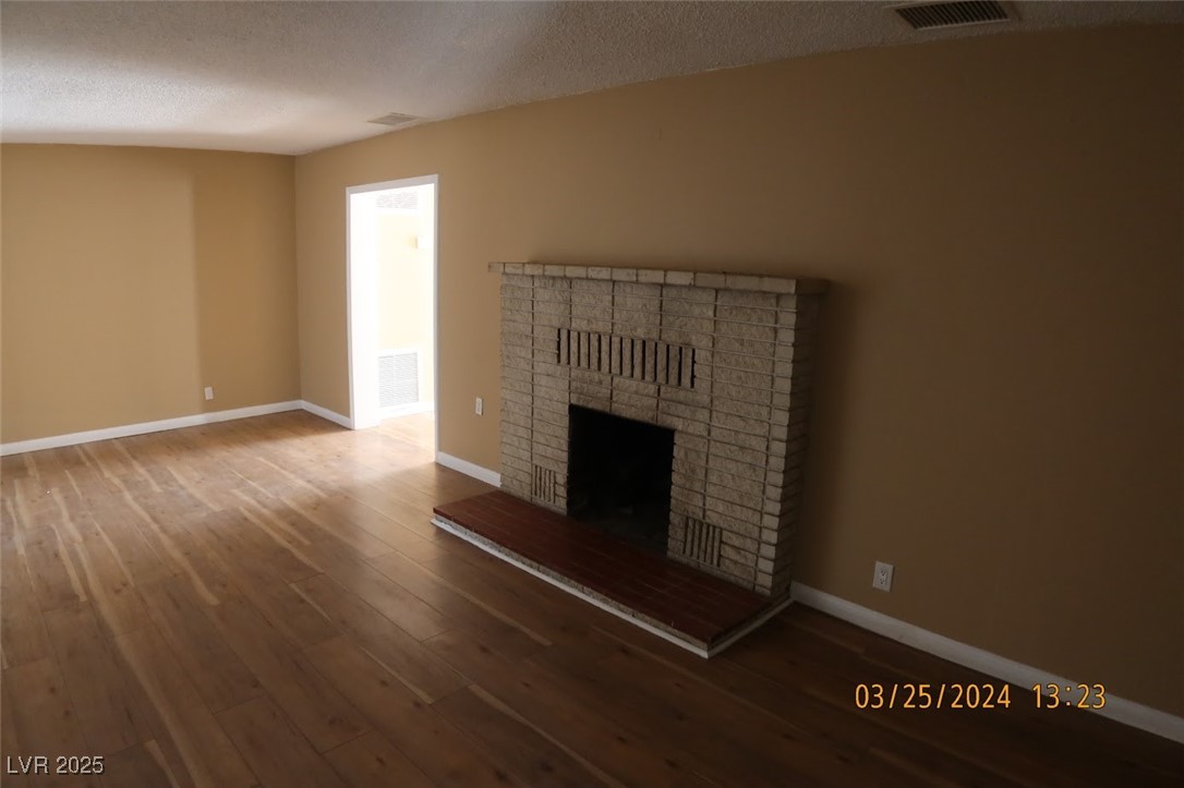 10 East Bonanza Road Las Vegas, NV 89101 - Photo 7 of 35 Unfurnished living room with wood-type flooring, baseboards, a brick fireplace, and visible vents