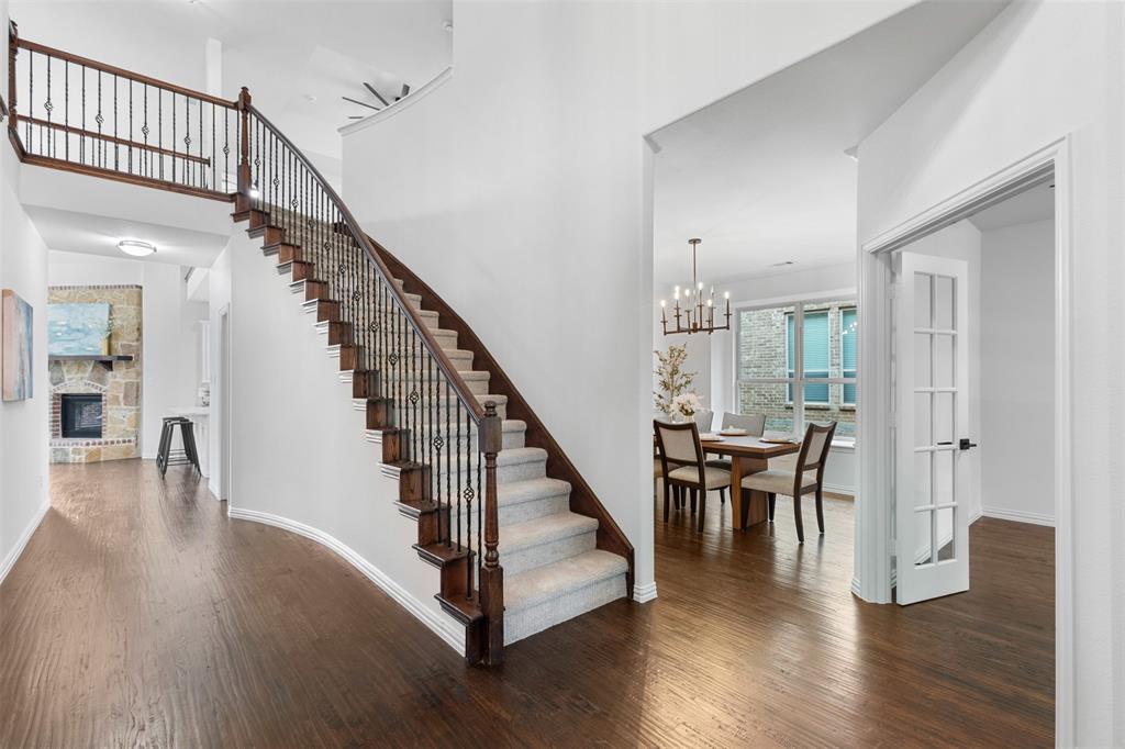 11984 Del Rio Drive Frisco, TX 75035 - Photo 4 of 38 Staircase with wood finished floors, an inviting chandelier, a fireplace, baseboards, and a towering ceiling