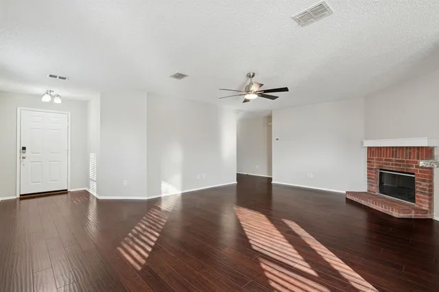 a view of an empty room with wooden floor fireplace and a window