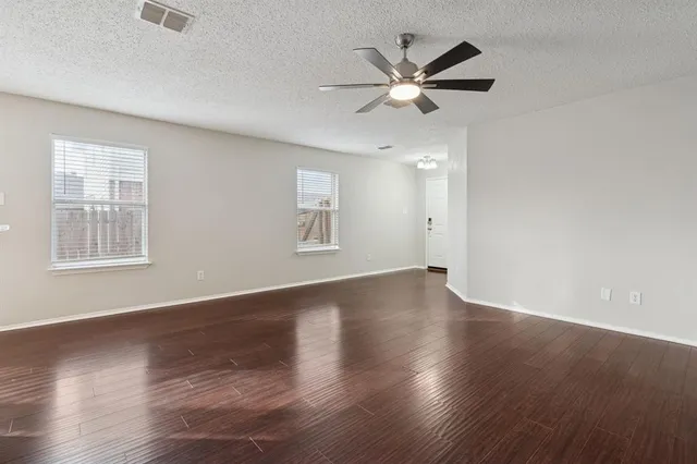 an empty room with wooden floor fan and windows