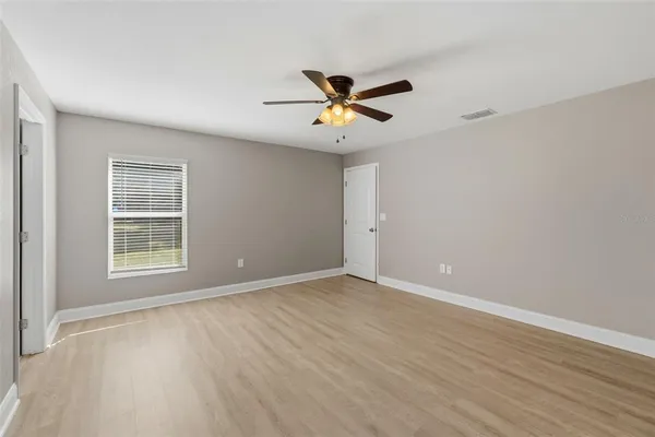 an empty room with wooden floor ceiling fan and windows