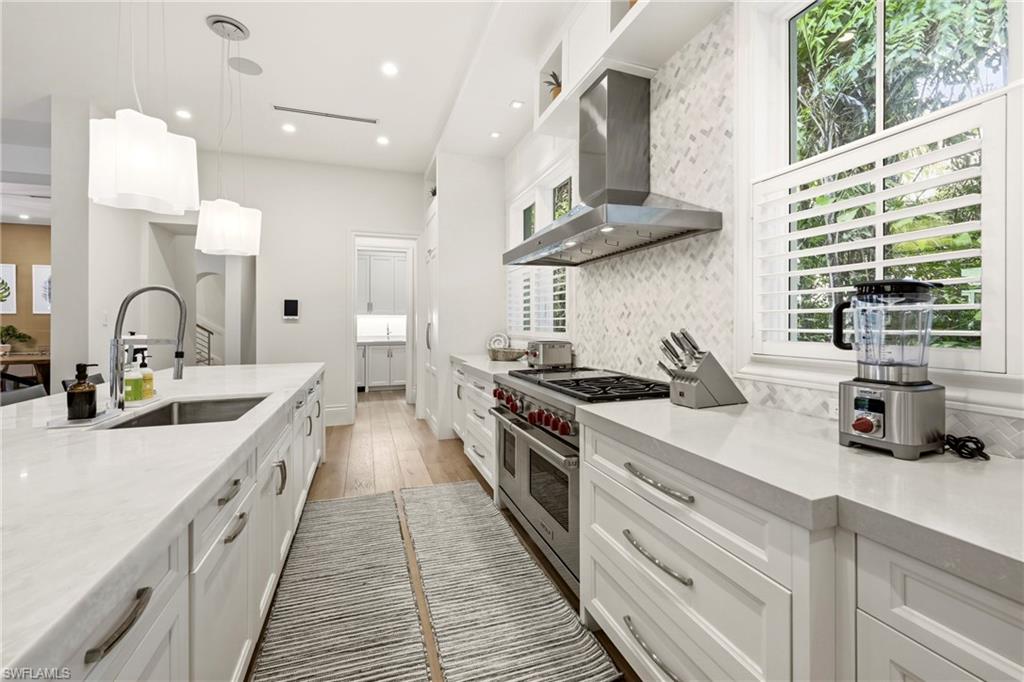 215 3rd Avenue North Naples, FL 34102 - Photo 10 of 47 Kitchen featuring light stone counters, white cabinetry, decorative light fixtures, double oven range, and light wood finished floors