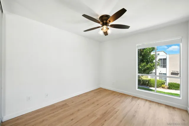 an empty room with wooden floor fan and windows