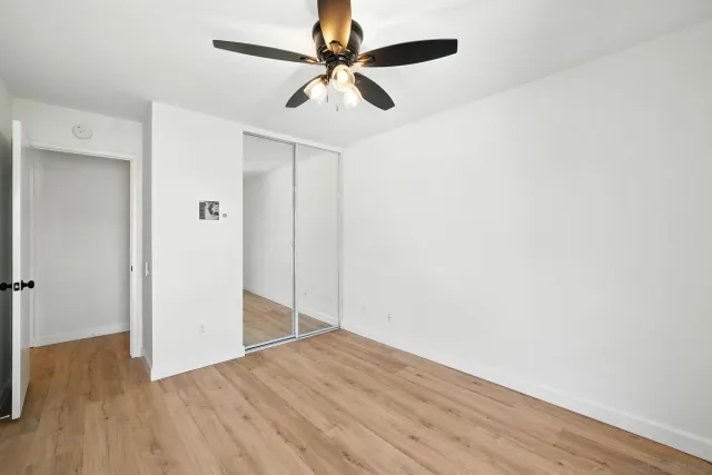 an empty room with wooden floor fan and windows