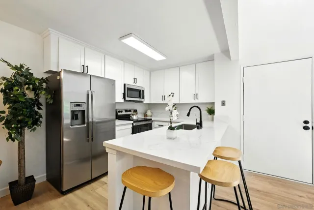 a kitchen with stainless steel appliances granite countertop a refrigerator a stove a sink dishwasher and white cabinets with wooden floor