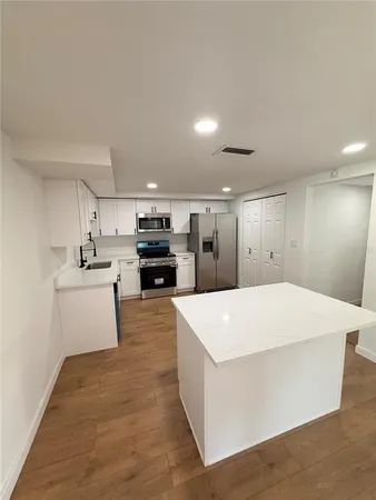 a large white kitchen with kitchen island a stove a sink a refrigerator and white cabinets with wooden floor