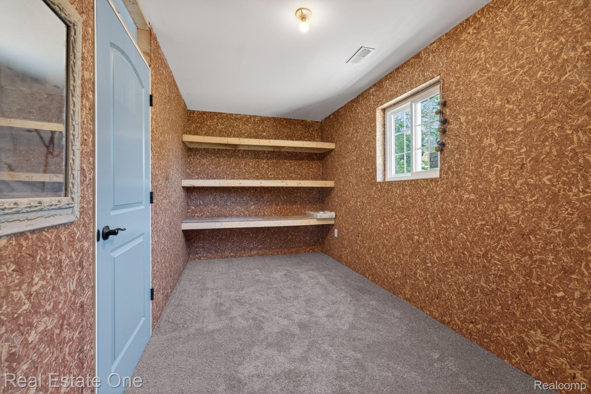 26987 Crawford Road Romulus, MI 48174 - Photo 33 of 51 Room featuring a light blue door with dark hardware, built-in wooden shelving, a window with exterior visibility, and grey carpet flooring