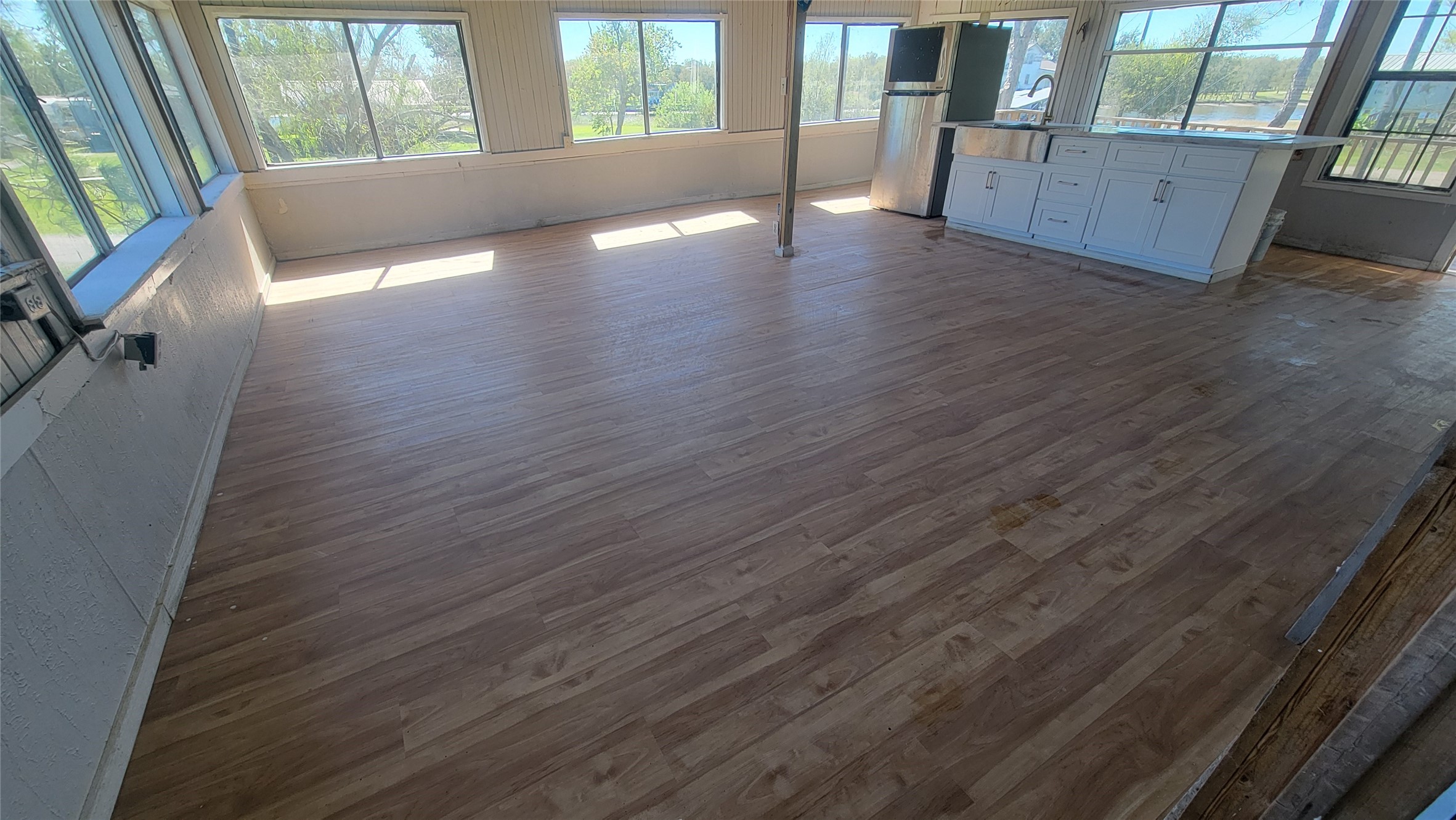 12018 Sandpiper Road Angleton, TX 77515 - Photo 12 of 48 This bright, open-concept room features expansive windows for natural light, hardwood flooring, and a modern kitchen area with white cabinetry and a small island. Ideal for entertaining or family living.