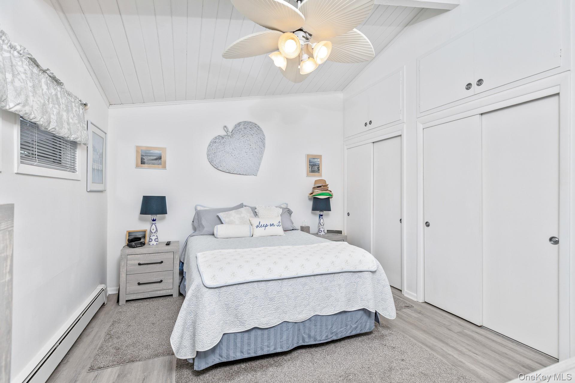 Vaulted ceiling with wood paneling, ceiling fan with integrated lighting, two sliding door closets, and wood-finish flooring