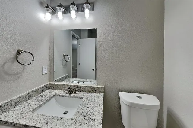 a bathroom with a granite countertop sink a toilet and a mirror