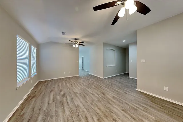 an empty room with wooden floor chandelier fan and windows