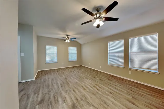 a view of an empty room with chandelier fan and wooden floor