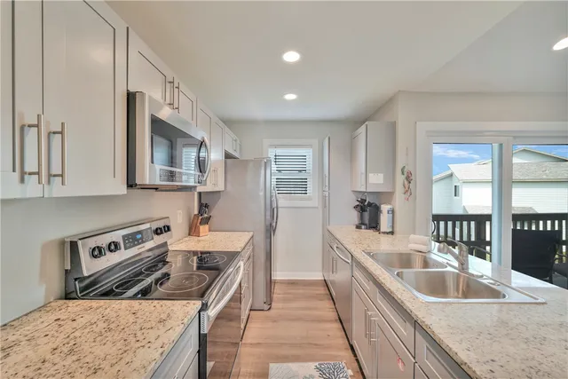 a kitchen with stainless steel appliances granite countertop a stove top oven a sink dishwasher and a refrigerator with wooden floor