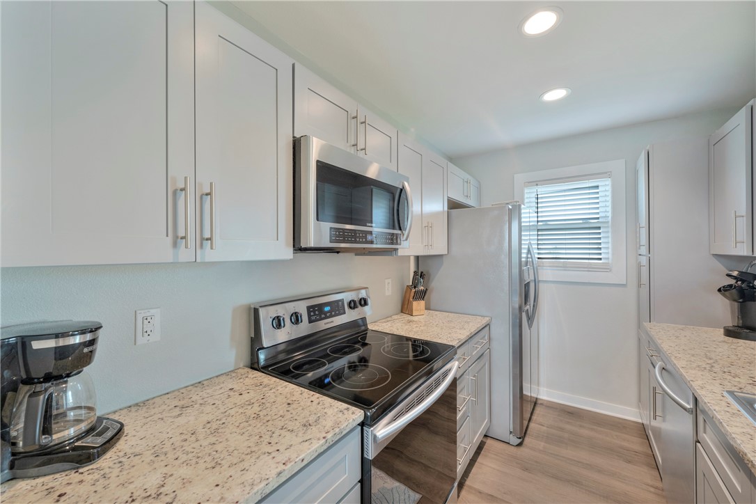 230 Cut-Off Road, Unit 204 Port Aransas, TX 78373 - Photo 10 of 37 a kitchen with stainless steel appliances granite countertop a stove top oven a sink dishwasher and a refrigerator with wooden floor